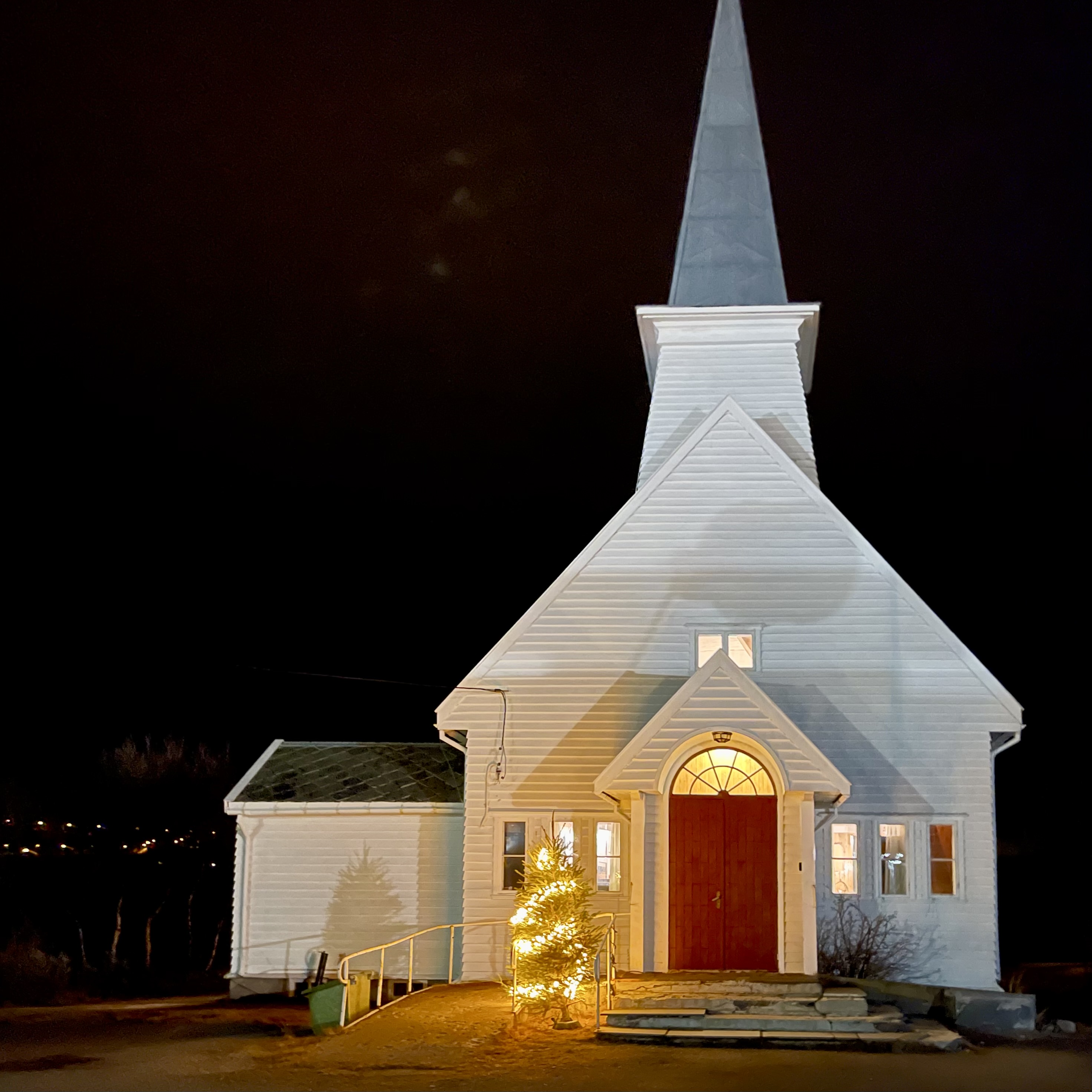 Vit kyrka med ljus på kvällen.