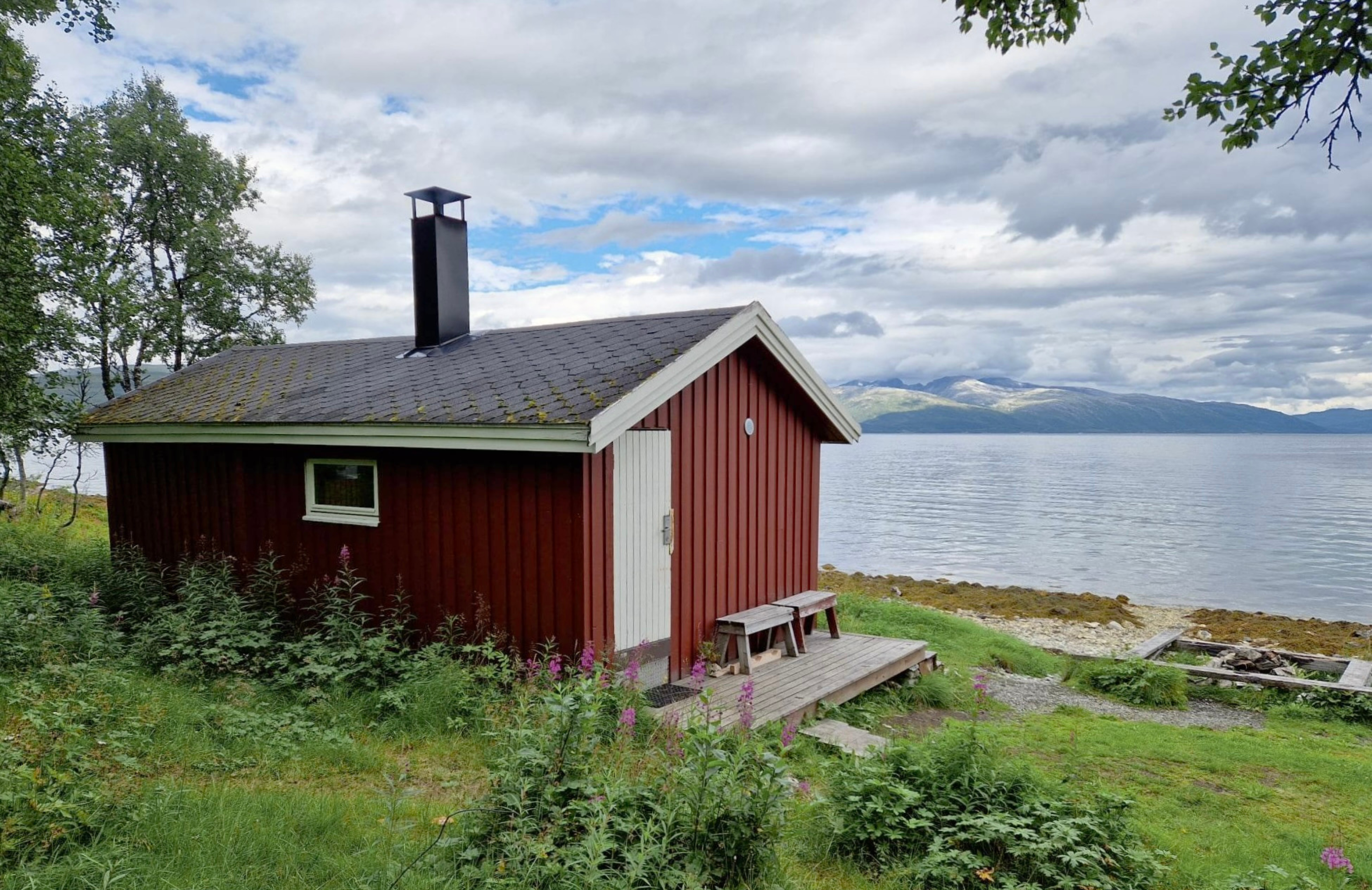 Bastu framför. Strand, vatten och berg i bakgrunden.