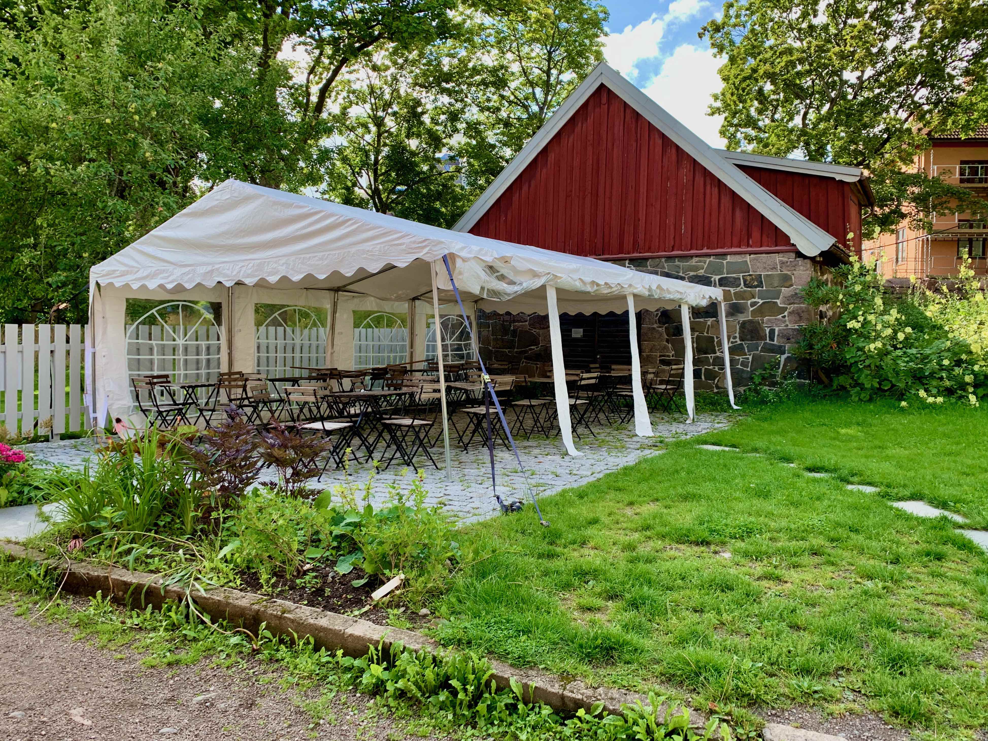 Oslo: Sommarkyrka i staden Bord och stolar i trädgården under en tak.